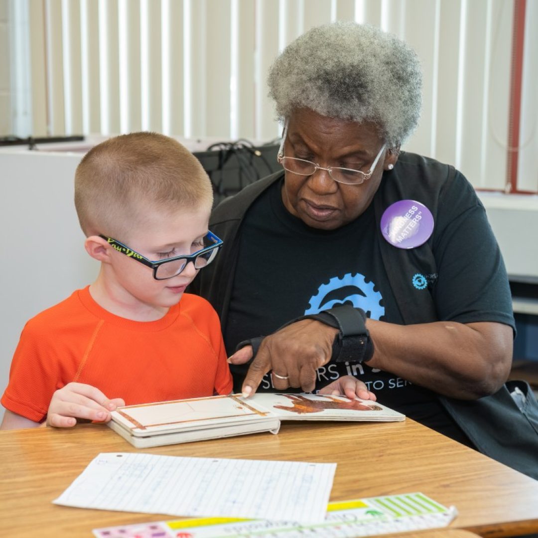 Seniors in Service Classroom Grandparent volunteer helping student learning sight words with book.